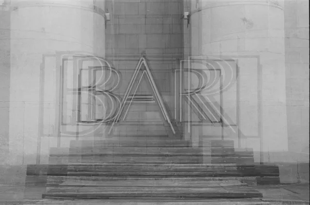 Czarno-białe zdjęcie neonu 'BAR' nałożonego na schody i kolumny.